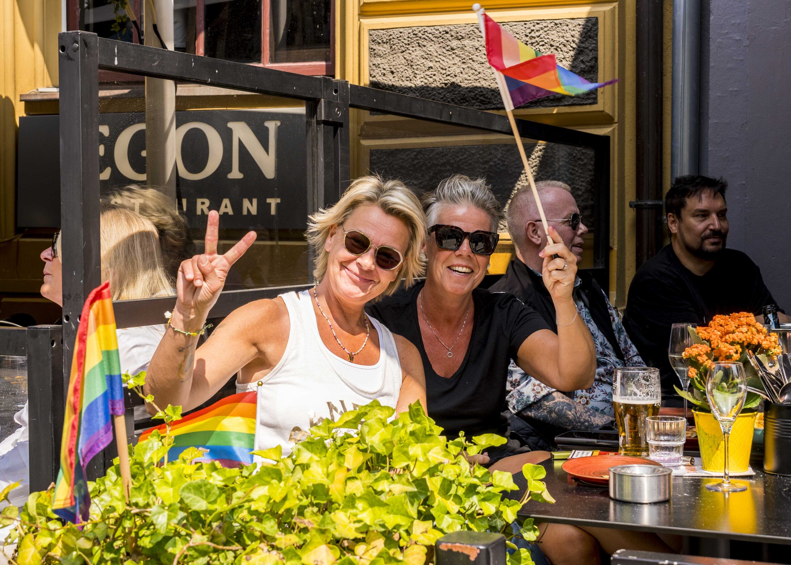 To damer med Pride flagg sittende utenfor Brødrene Bergh.