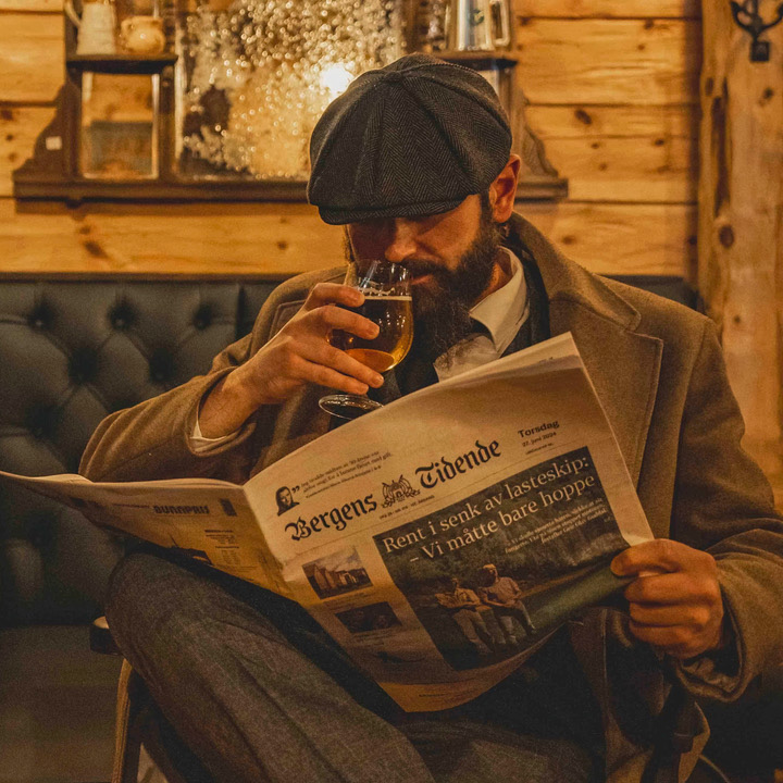 En mann som sitter og leser en avis og drikker øl