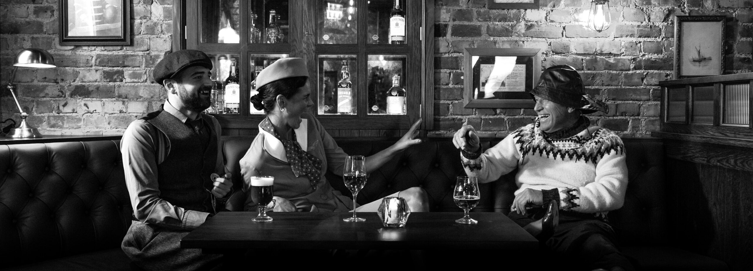 To menn og en kvinne som sitter i en bås i en pub og drikker og ler